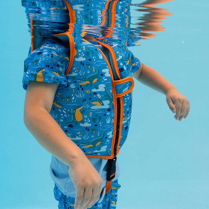 Little one wearing swim vest with non-removable floats in blue, bright orange trims, and crocodiles and frogs themed print. Open.