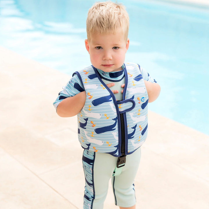 Lifestyle image of child wearing neoprene swim vest with non-removable floats in light blue, navy trims, and whales and anchors themed print. Front.