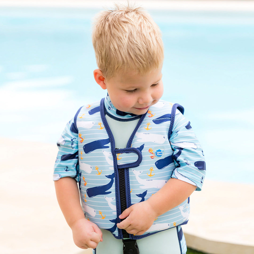 Lifestyle image of child wearing neoprene swim vest with non-removable floats in light blue, navy trims, and whales and anchors themed print. Front.