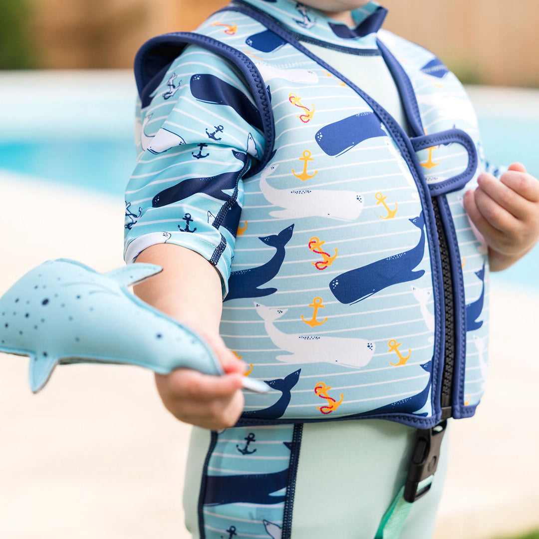 Lifestyle image of child wearing neoprene swim vest with non-removable floats in light blue, navy trims, and whales and anchors themed print. Side.