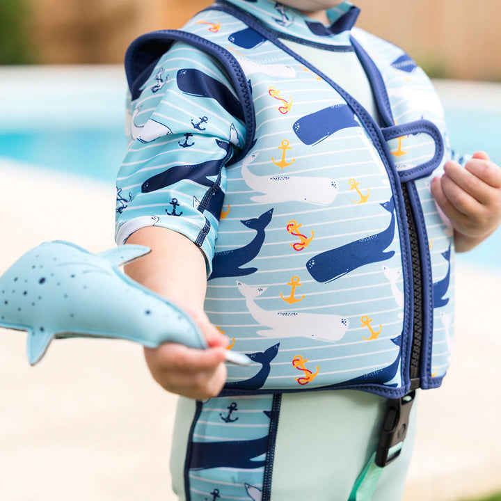 Lifestyle image of child wearing neoprene swim vest with non-removable floats in light blue, navy trims, and whales and anchors themed print. Side.