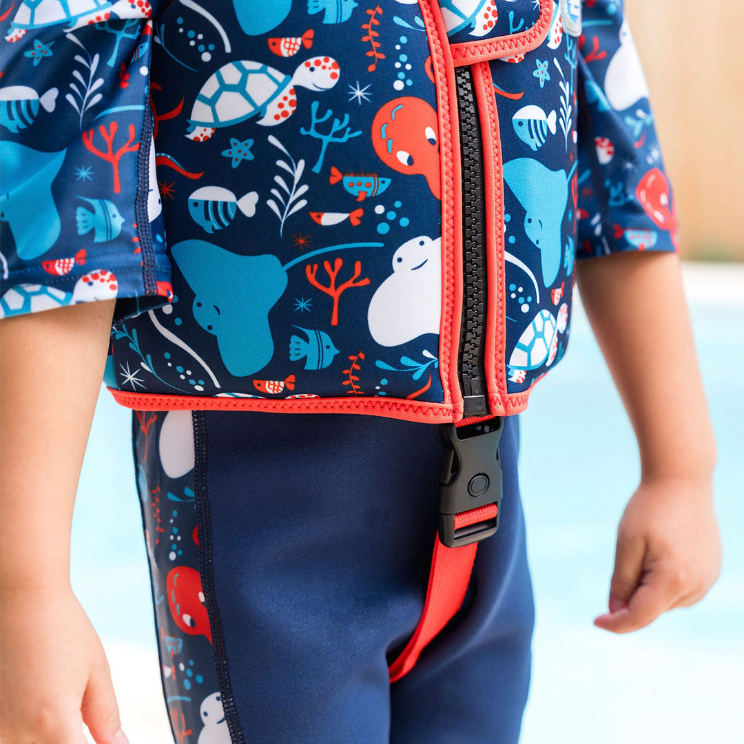 Lifestyle image of child wearing neoprene swim vest with non-removable floats in navy, red trims, and sea life themed print. Front.