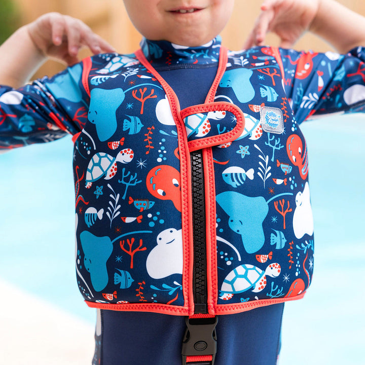 Lifestyle image of child wearing neoprene swim vest with non-removable floats in navy, red trims, and sea life themed print. Front.