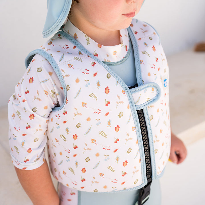 Lifestyle image of child wearing neoprene swim vest with non-removable floats in white, light blue trims, and Autumn themed print. Side.