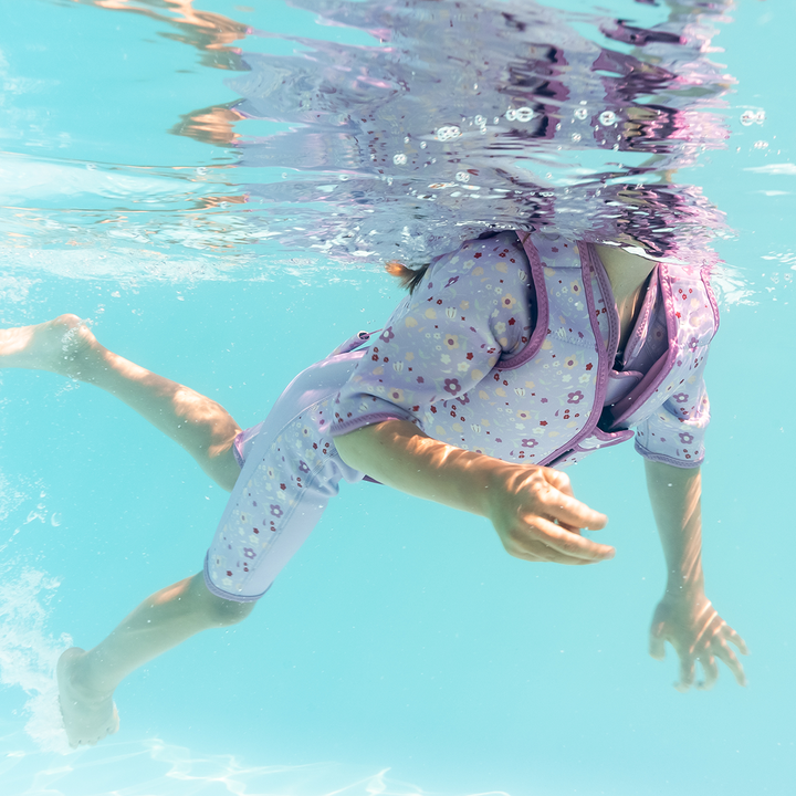 Lifestyle image of child swimming with neoprene swim vest with non-removable floats in lilac, and floral print.