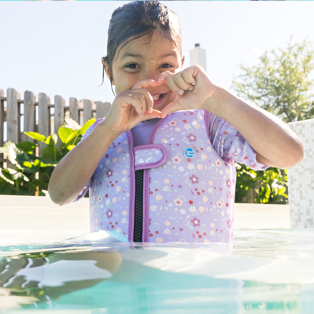 Lifestyle image of child wearing neoprene swim vest with non-removable floats in lilac, and floral print. Front.