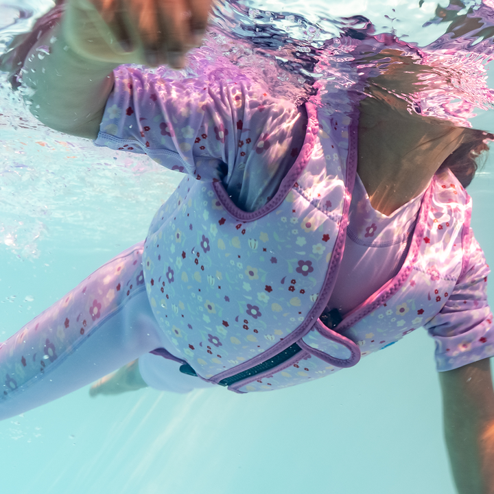 Lifestyle image of child swimming with neoprene swim vest with non-removable floats in lilac, and floral print.