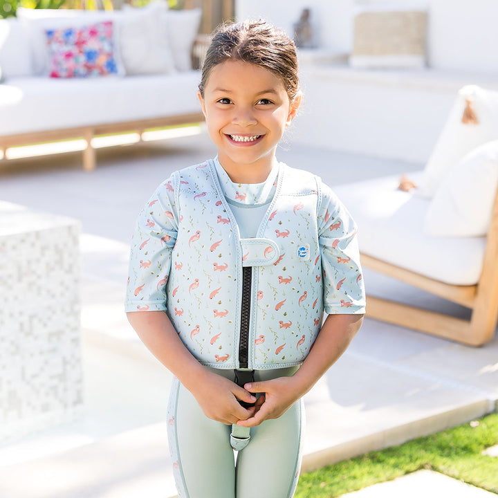 Lifestyle image of child wearing neoprene swim vest with non-removable floats in light blue, navy trims, and otters themed print. Front.