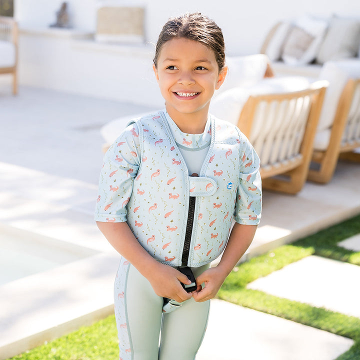 Lifestyle image of child wearing neoprene swim vest with non-removable floats in light blue, navy trims, and otters themed print. Front.