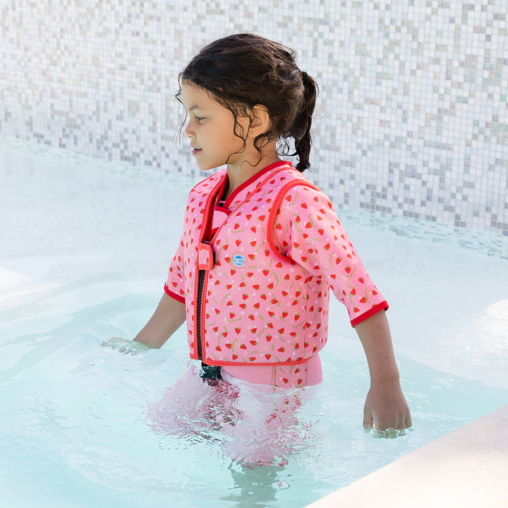Lifestyle image of child wearing neoprene swim vest with non-removable floats in pink, red trims and strawberries themed print. Side.