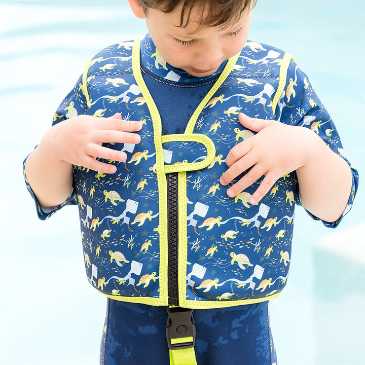 Little one wearing swim vest for toddlers with non-removable floats in navy, bright green trims, and turtles and mantarays themed print.