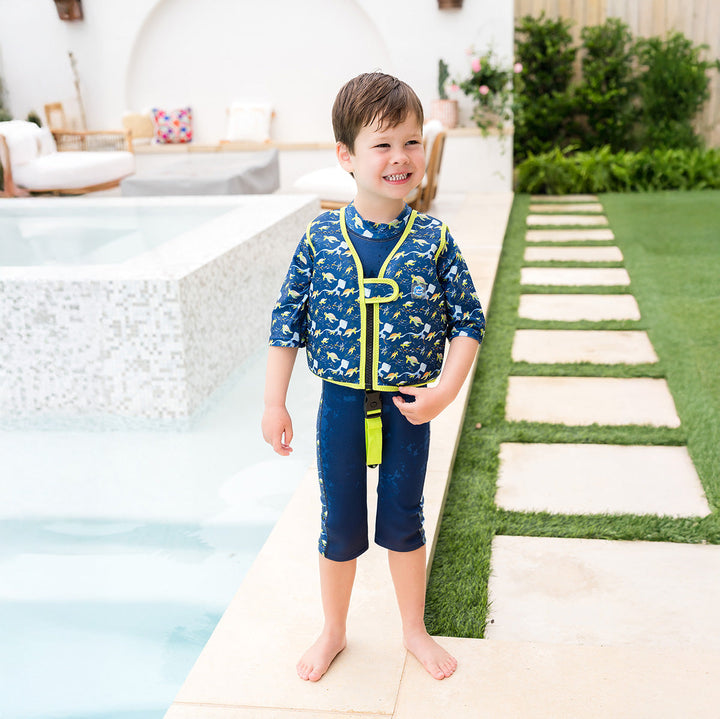 Little one wearing swim vest for toddlers with non-removable floats in navy, bright green trims, and turtles and mantarays themed print.