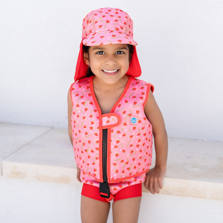 Lifestyle image of child wearing neoprene swim vest with non-removable floats in pink, red trims and strawberries themed print. Front.