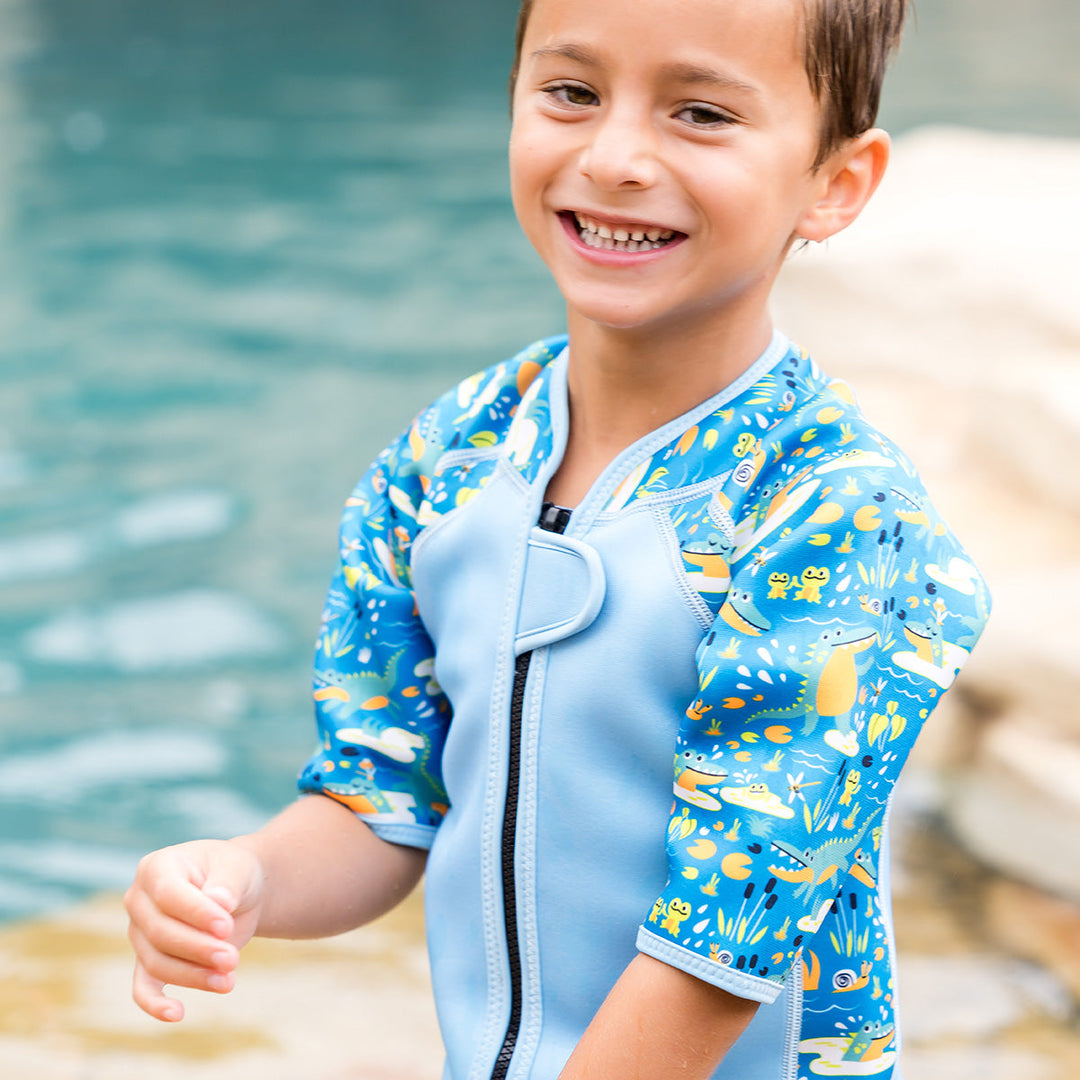 Kid wearing shorty wetsuit in light blue featuring crocodiles and frogs themed print in sleeves and side panels.