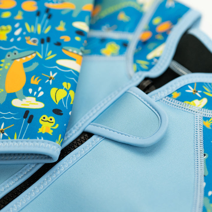 Shorty wetsuit in light blue featuring crocodiles and frogs themed print in sleeves and side panels. Close-up of the front zip.