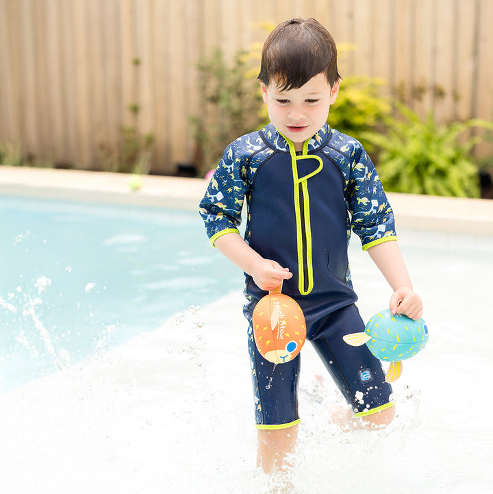 Kid wearing a shorty wetsuit in navy with bright green trims, featuring turtles and mantarays themed print in sleeves and side panels.
