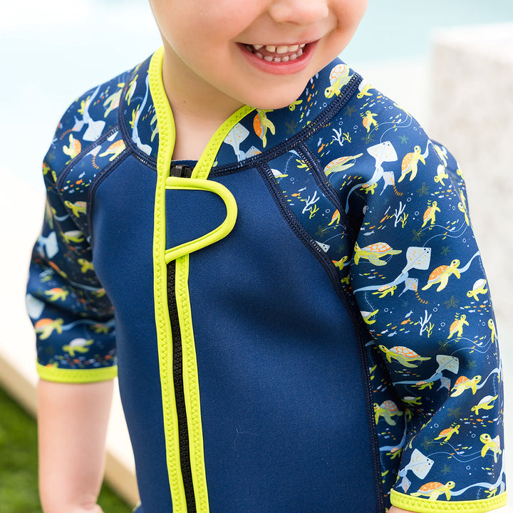 Close-up of front zip in the shorty wetsuit in navy with bright green trims, featuring turtles and mantarays themed print in sleeves and side panels.