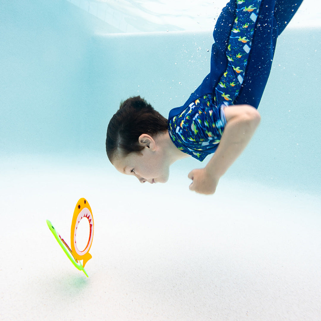 Kid diving to retrieve shark dive rings standing at the bottom of the pool