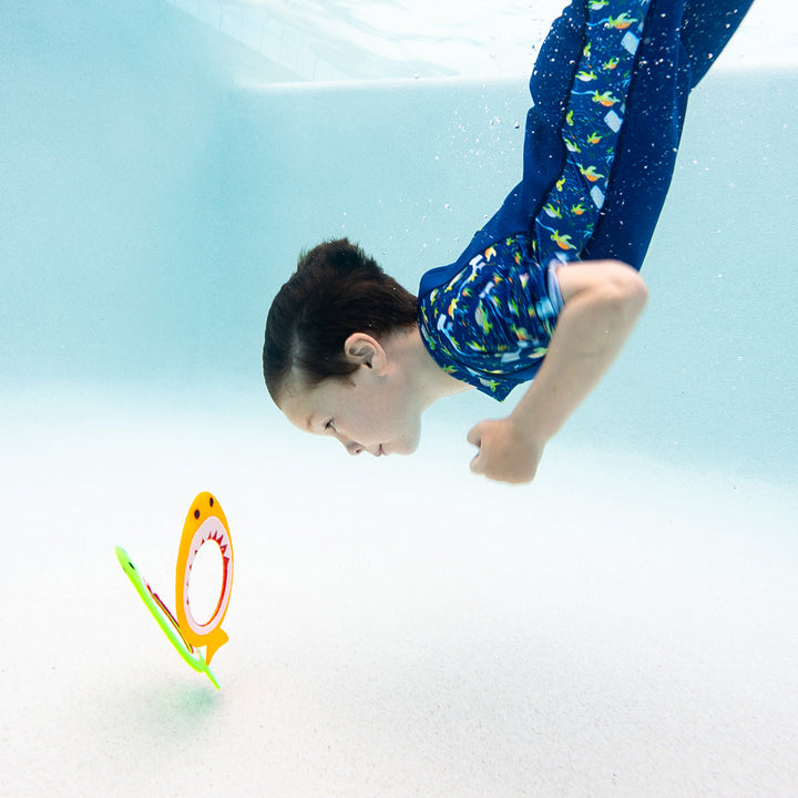 Kid diving to retrieve shark dive rings standing at the bottom of the pool
