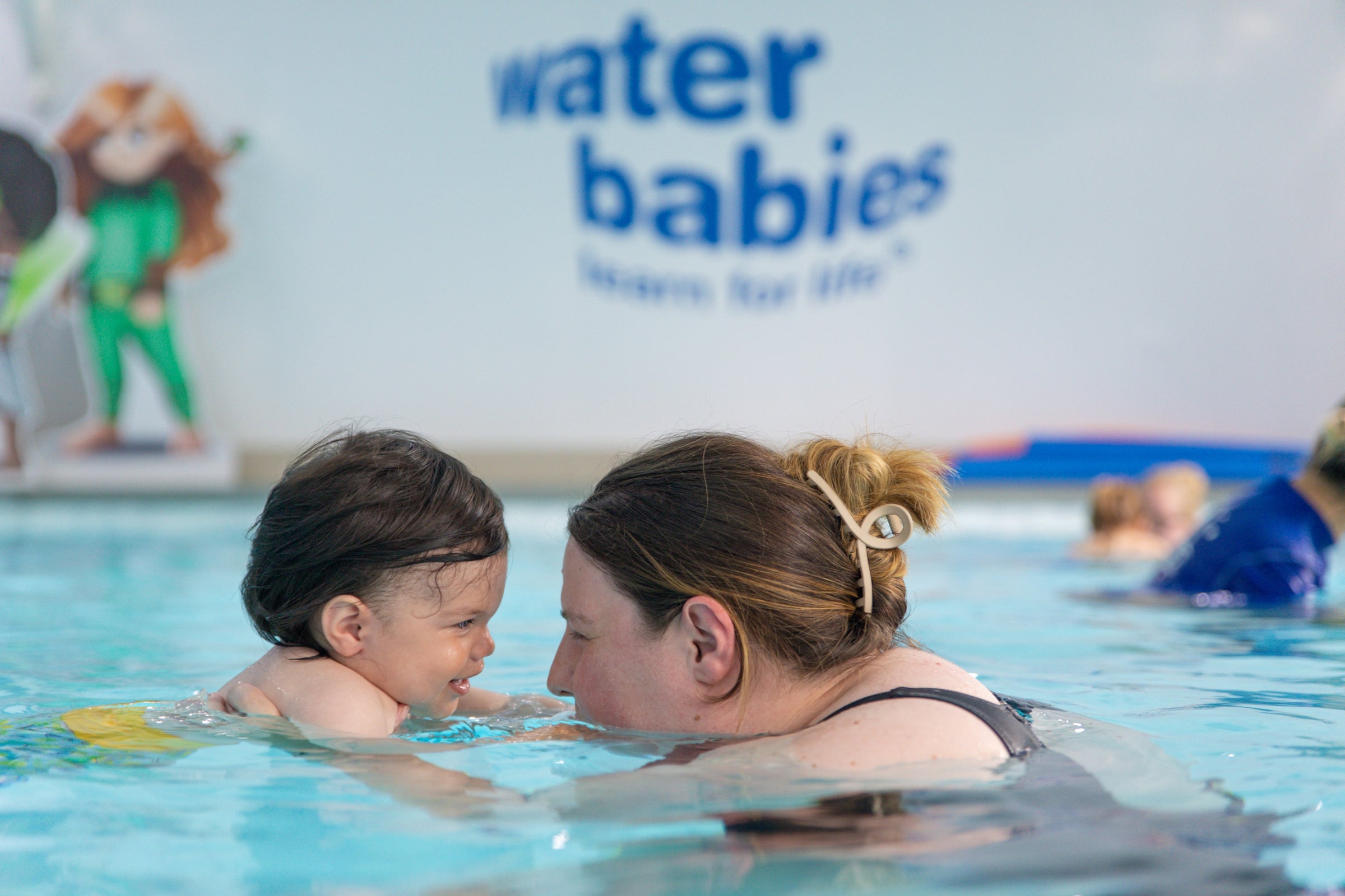 Woman and child in a pool with 'Water Babies' branding in the background