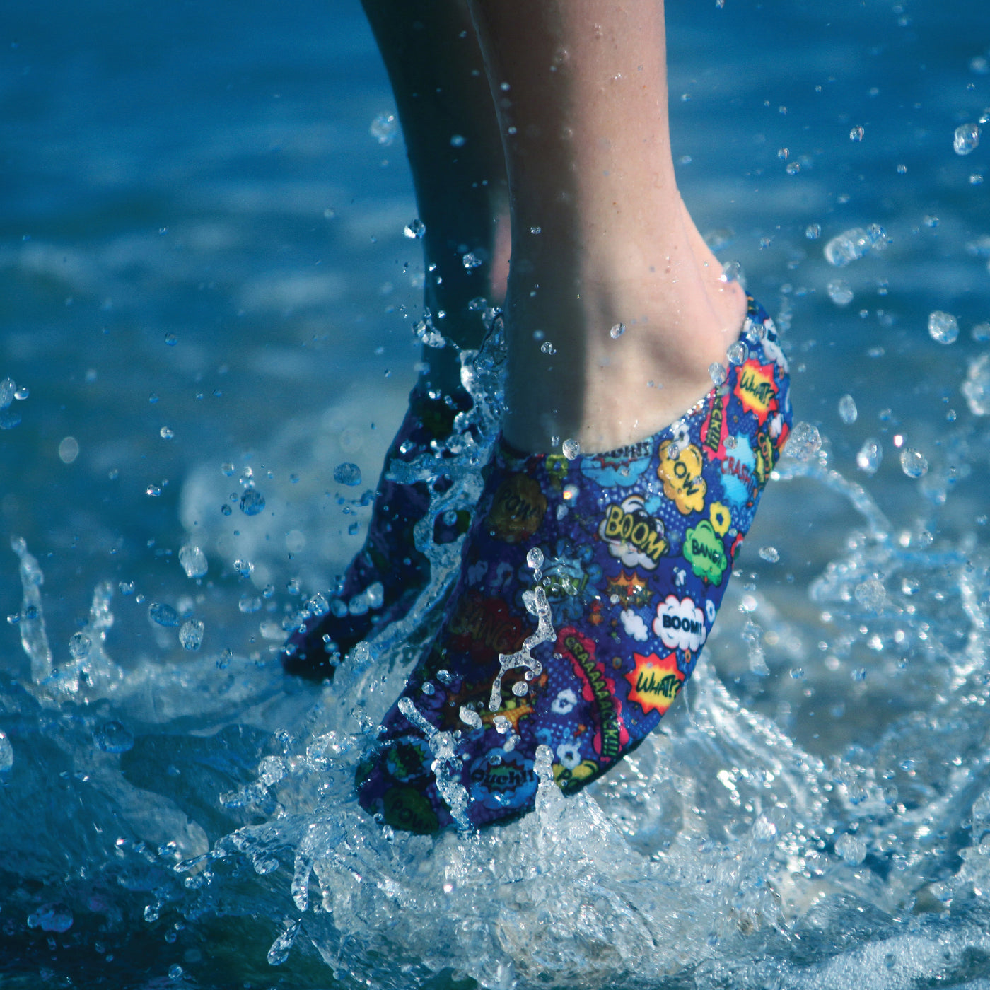 Lifestyle image of kid wearing superhero themed water shoes, jumping in the sea.