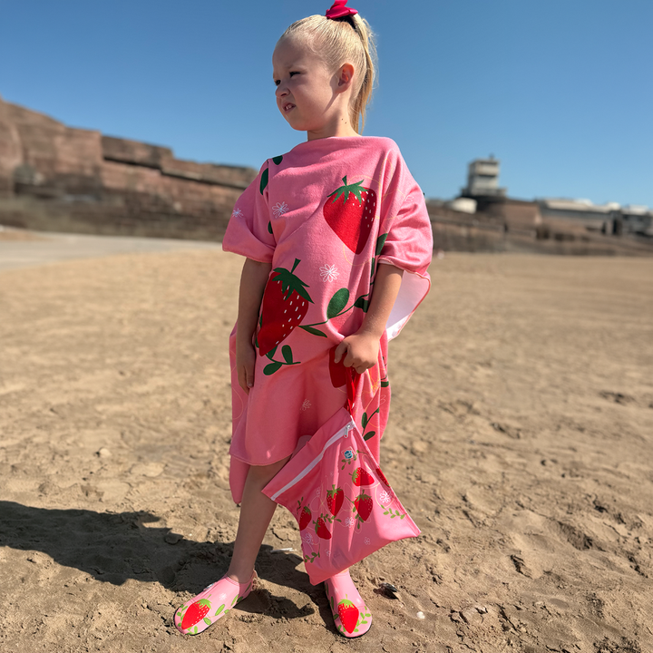 Little one wearing hooded poncho in red and pink with strawberries themed print.