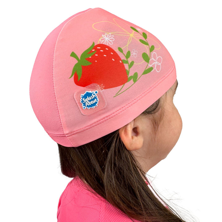 Little one wearing baby swim hat in pink featuring strawberries themed print.
