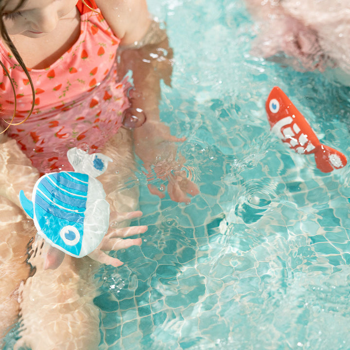 Kid playing with red and white silicone fish in the pool