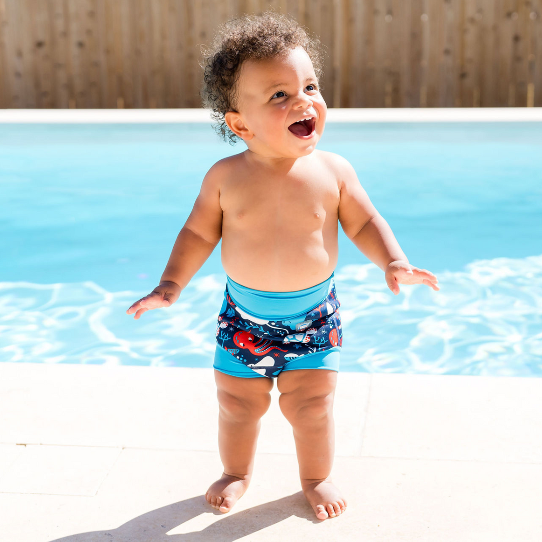 Child wearing reusable swim nappy in navy with cyan ribs and sea creatures themed print. Front.