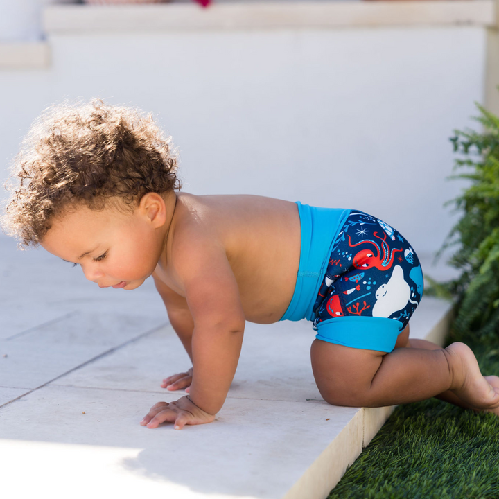 Child wearing reusable swim nappy in navy with cyan ribs and sea creatures themed print. Side.
