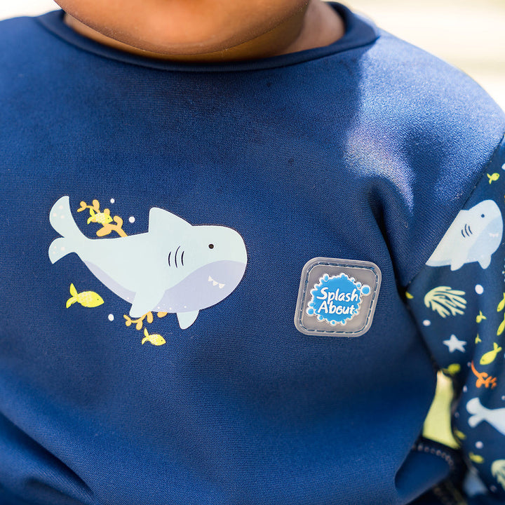 Little one wearing fleece-lined baby wetsuit in navy with sharks themed print.