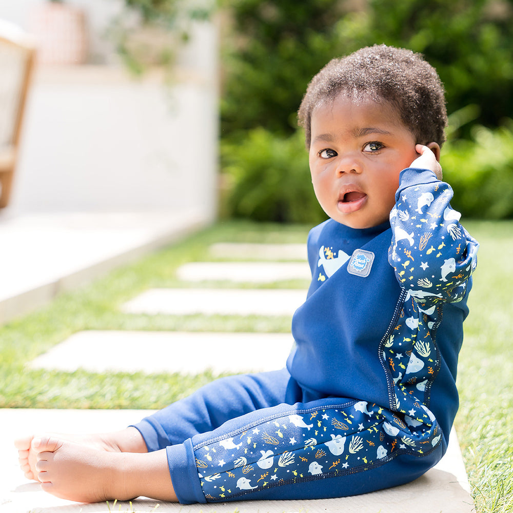 Little one wearing fleece-lined baby wetsuit in navy with sharks themed print.