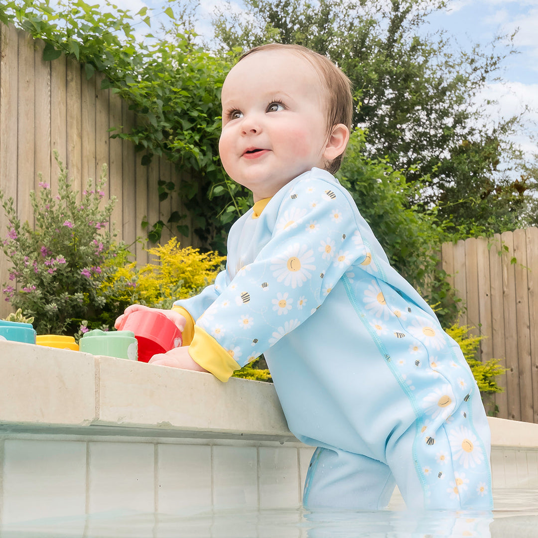 Little one wearing fleece-lined baby wetsuit in baby blue with yellow trims and daisies themed print.