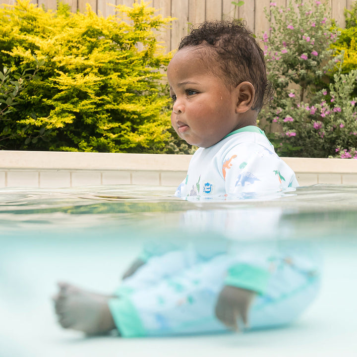 Little one wearing fleece-lined baby wetsuit in baby blue with mint trims and dinosaurs themed print.