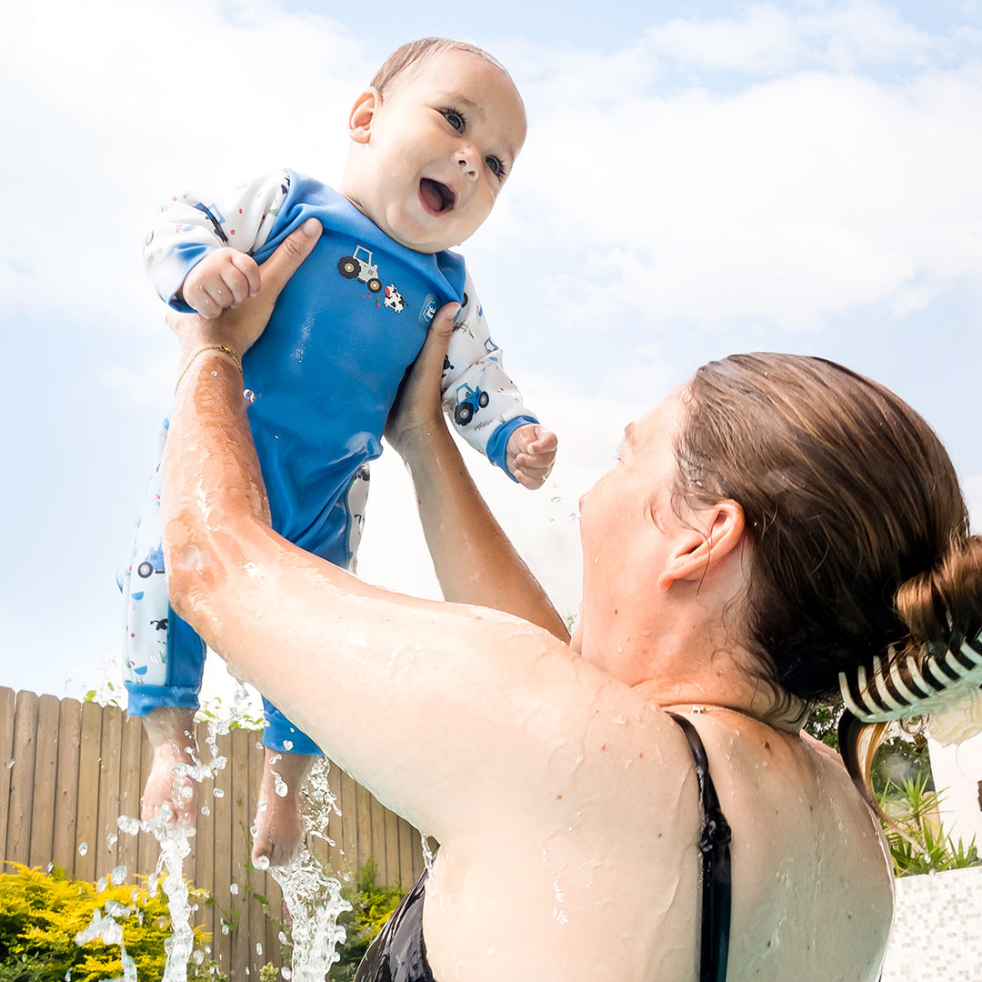 Little one wearing fleece-lined baby wetsuit in white and blue with farm themed print.