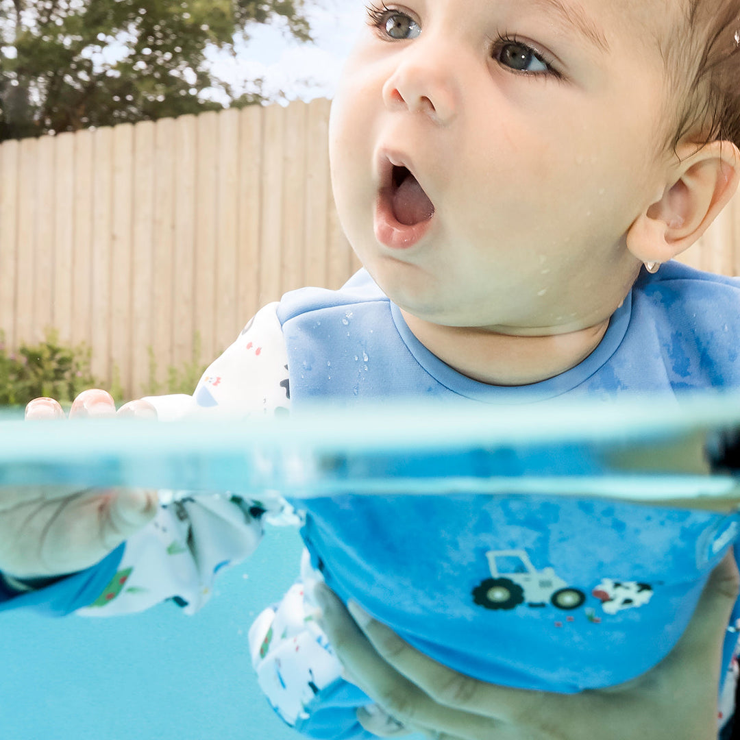 Little one wearing fleece-lined baby wetsuit in white and blue with farm themed print.