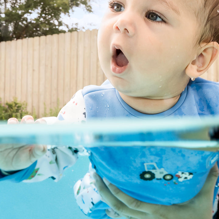 Little one wearing fleece-lined baby wetsuit in white and blue with farm themed print.