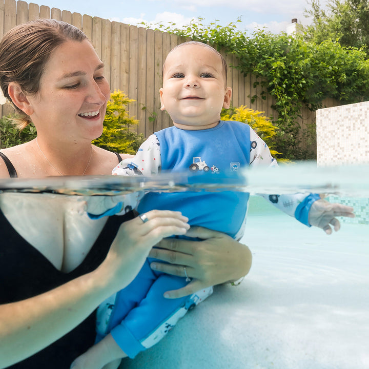 Little one wearing fleece-lined baby wetsuit in white and blue with farm themed print.