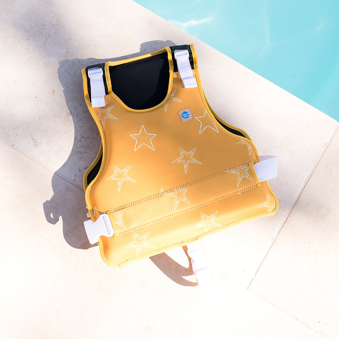 Neoprene swim vest for children with non-removable floats in bright yellow, and white stars themed print, poolside.