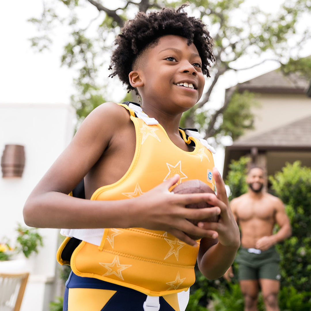 Child wearing neoprene swim vest with non-removable floats in bright yellow, and white stars themed print.