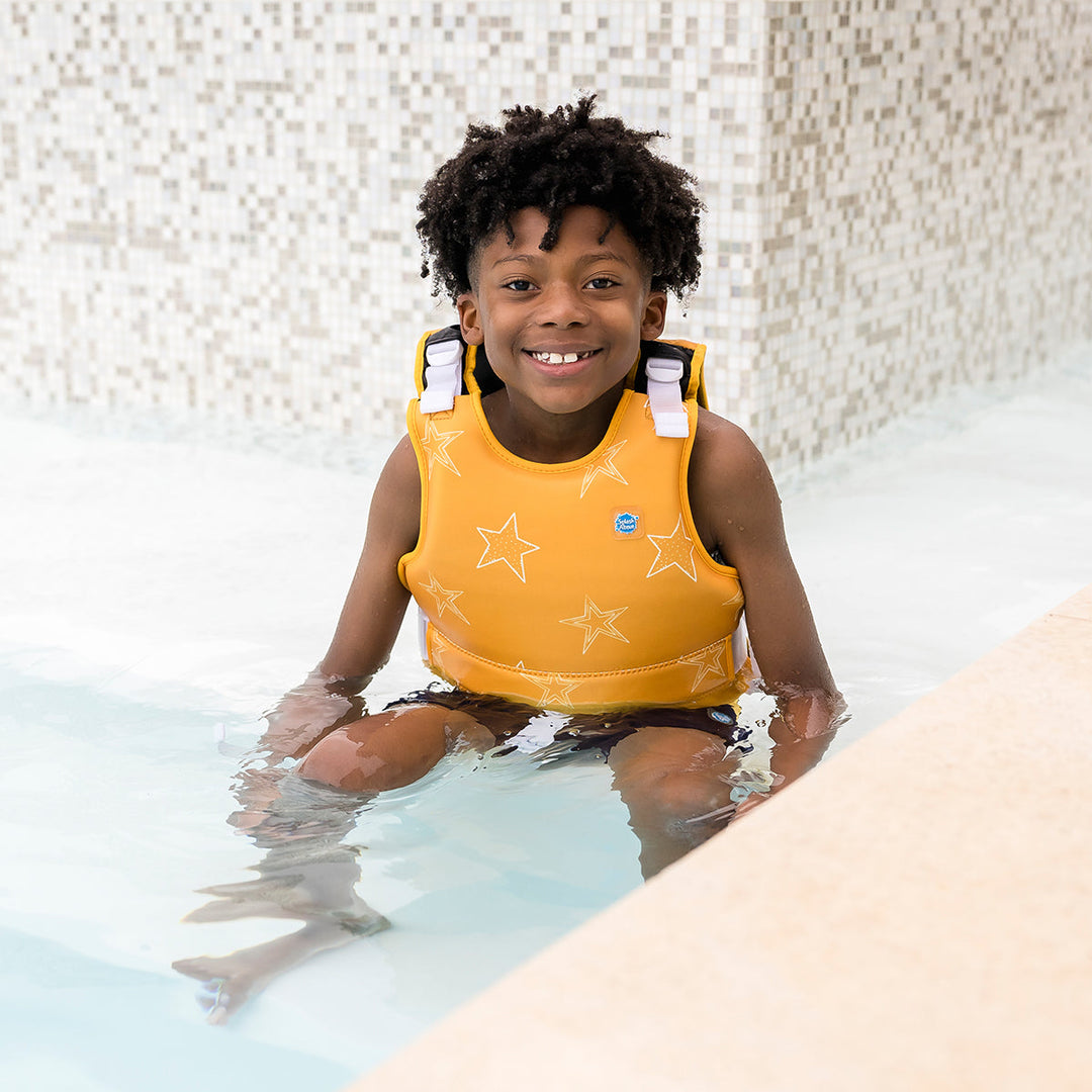 Child wearing neoprene swim vest in the pool with non-removable floats in bright yellow, and white stars themed print.