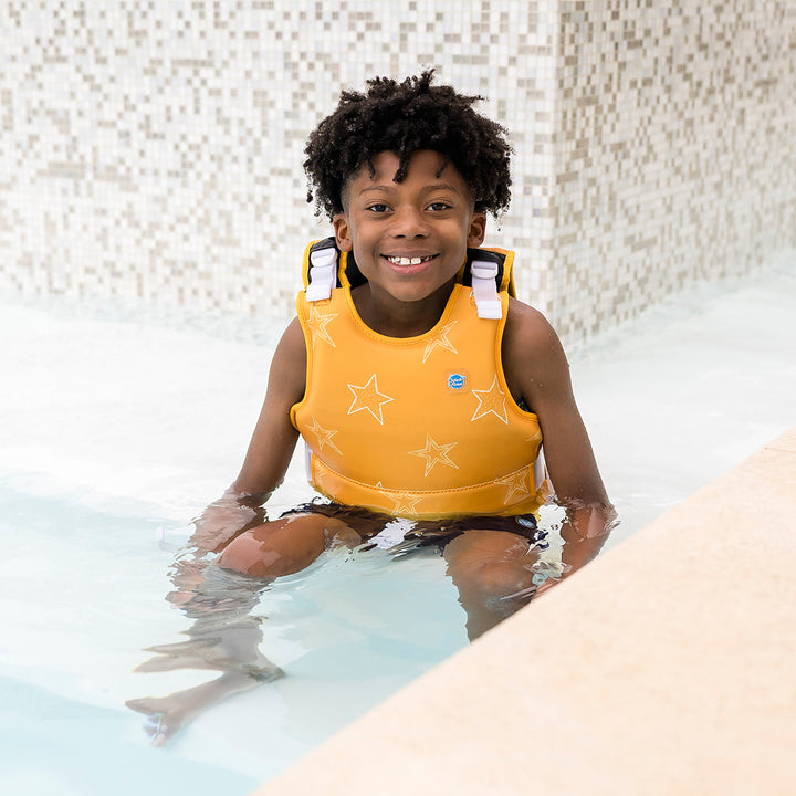Child wearing neoprene swim vest in the pool with non-removable floats in bright yellow, and white stars themed print.