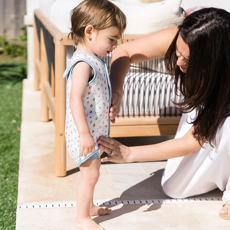 Child wearing neoprene baby wrap wetsuit in white with blue trims and autumn themed print.