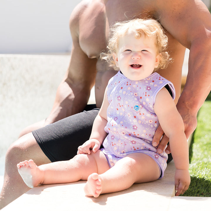 Child wearing neoprene baby wrap wetsuit in lilac with floral print.
