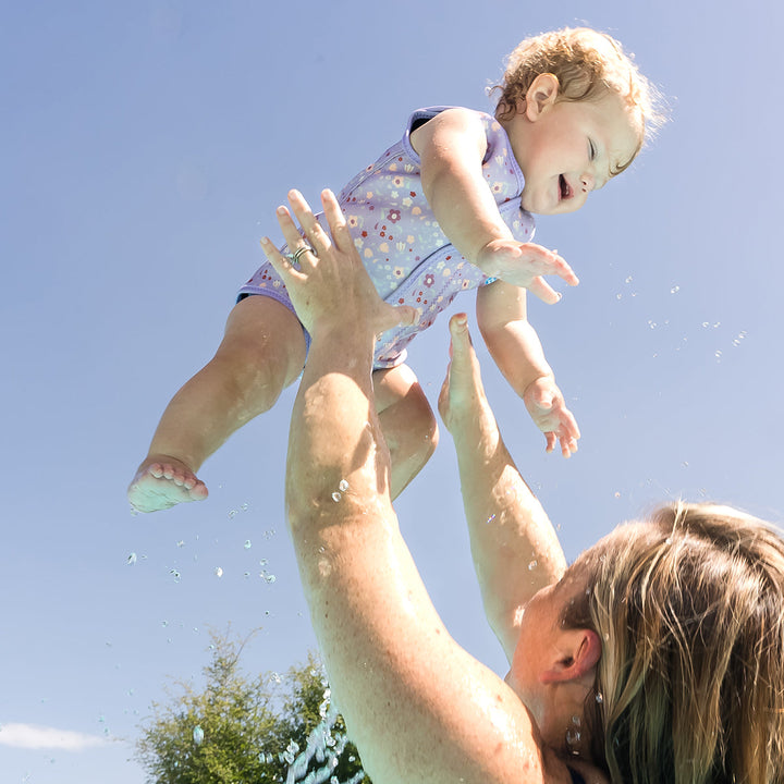 Child wearing neoprene baby wrap wetsuit in lilac with floral print.