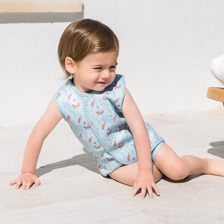 Child wearing neoprene baby wrap wetsuit in baby blue and otters themed print.