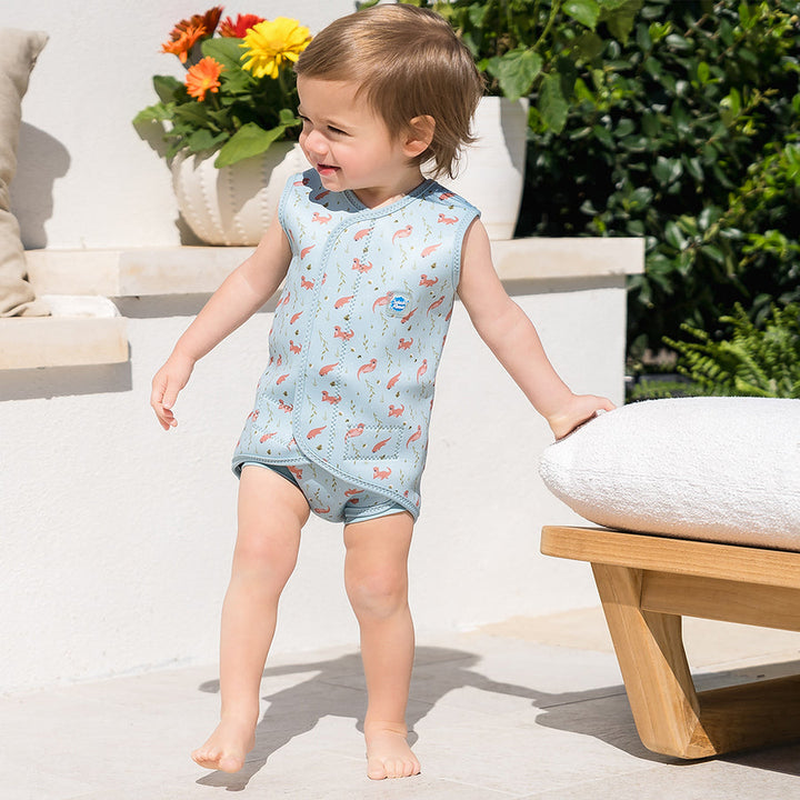 Child wearing neoprene baby wrap wetsuit in baby blue and otters themed print.