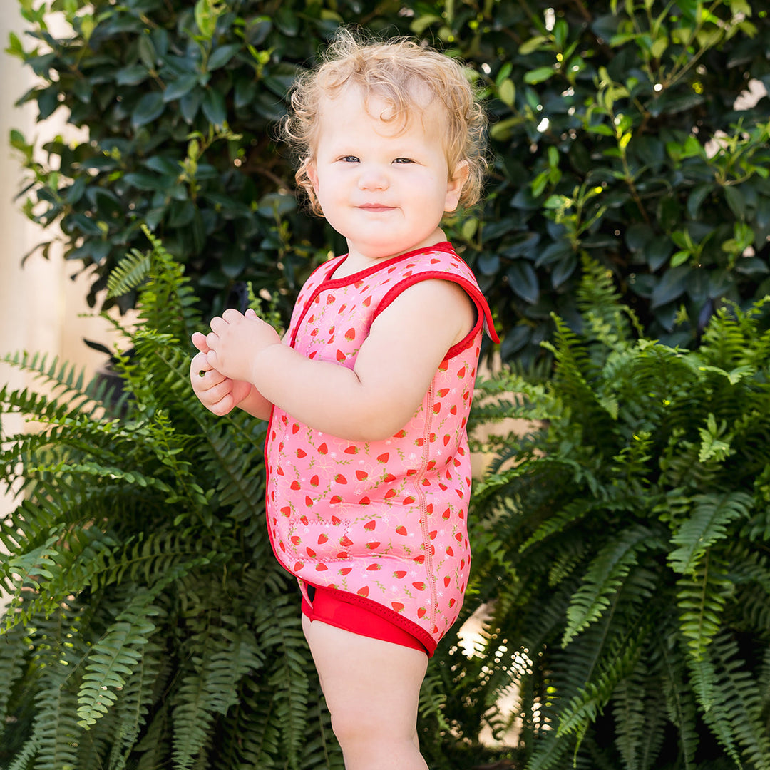Child wearing neoprene baby wrap wetsuit in pink and red with strawberries themed print.