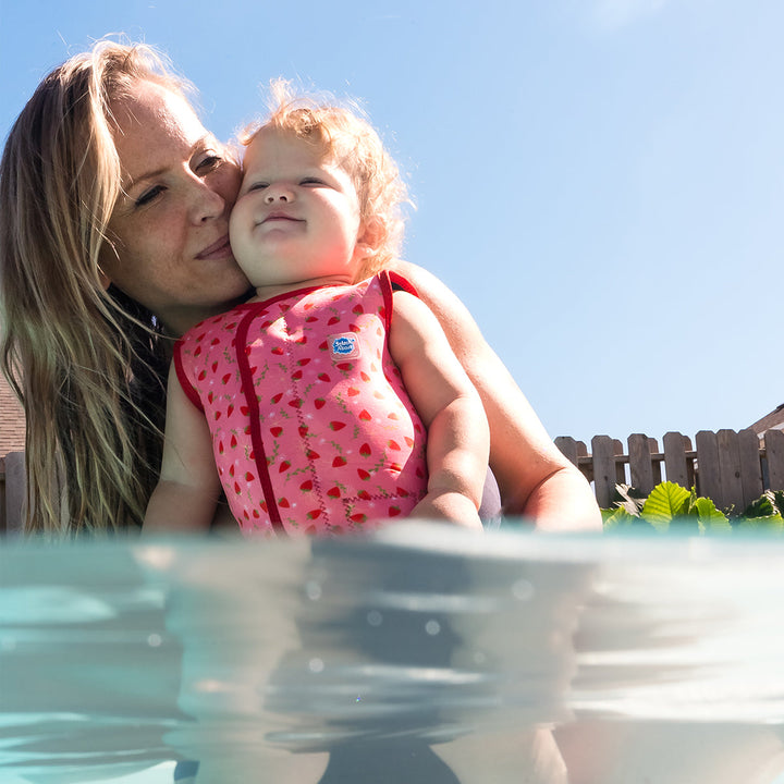 Child wearing neoprene baby wrap wetsuit in pink and red with strawberries themed print.