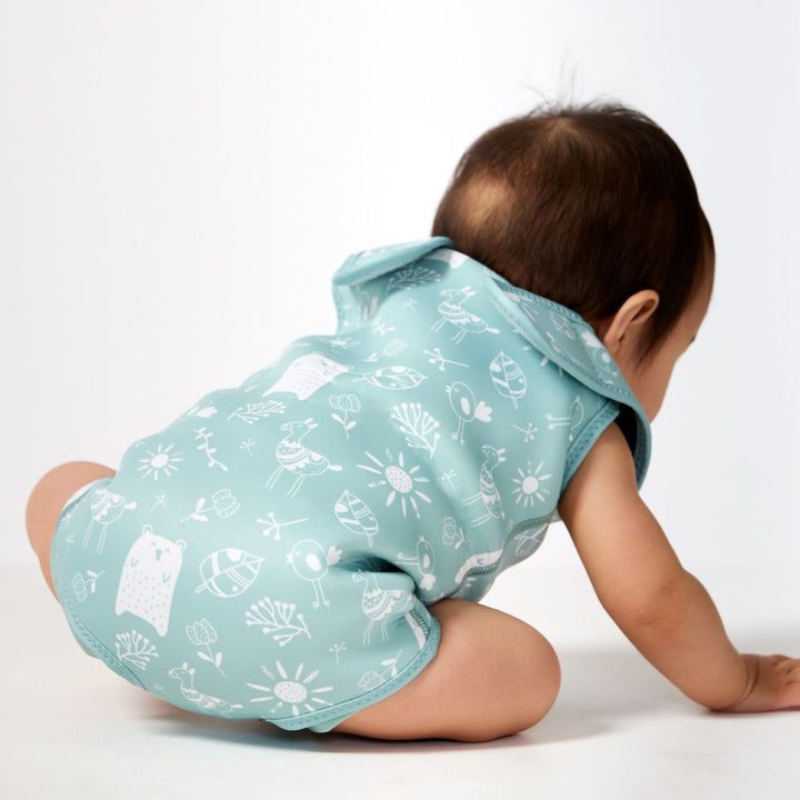 Little one wearing a neoprene baby wrap wetsuit in greenish blue with animals themed print, including bears, llamas, birds, suns and flowers. Back.